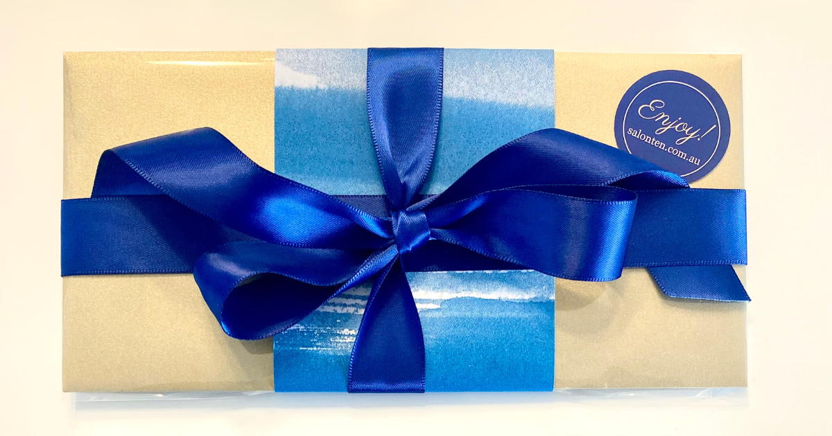 A Salon Ten gift voucher wrapped in gold paper with a navy satin ribbon and an Enjoy! sticker